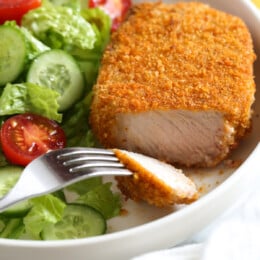 Breaded air fryer pork chops with lettuce, tomatoes, cucumbers, and a fork