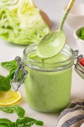 Spoonful of basil green goddess dressing dripping into jar