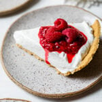 Slice of creamy no-bake cheesecake topped with macerated and fresh raspberries